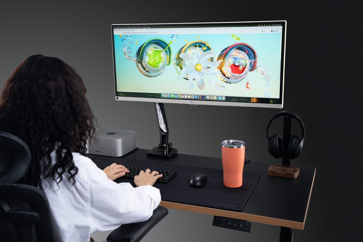 Người dùng ngồi làm việc trước màn hình LG ultrawide gắn arm màn hình trên bàn nâng hạ, kết hợp ghế công thái học.